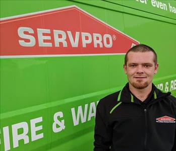 Male employee Alan (AJ) standing in front of green SERVPRO van